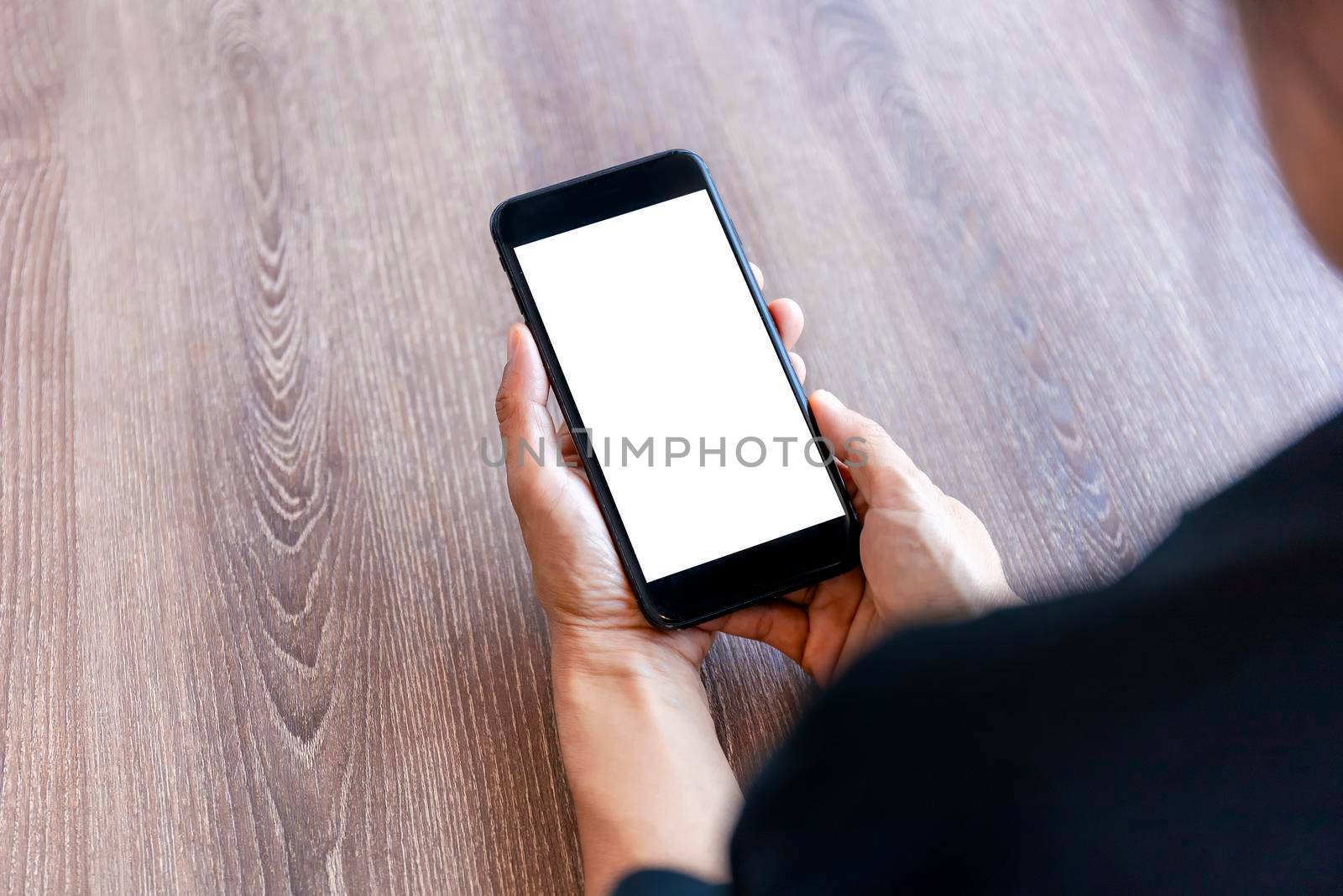 Top view female hands holding smart phone with blank white screen. Women hands workspace, close-up hand holding smartphone blank screen for text and content on wood table background.