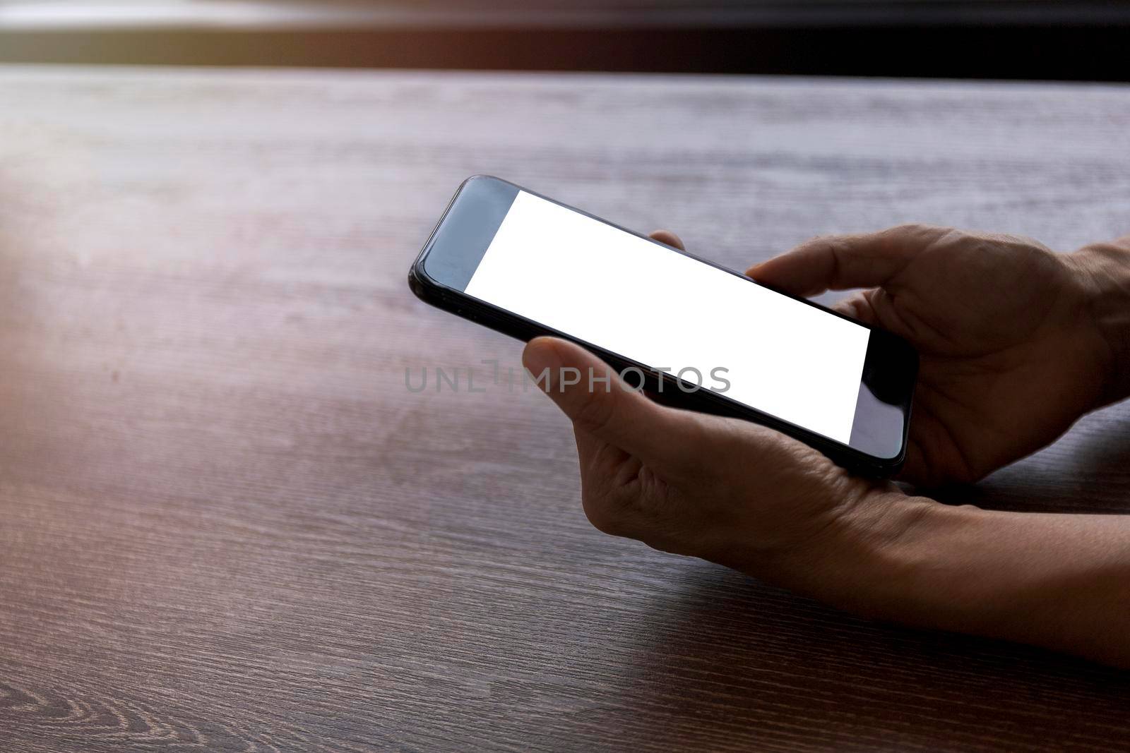 Top view female hands holding smart phone with blank white screen. Women hands workspace, close-up hand holding smartphone blank screen for text and content on wood table background.