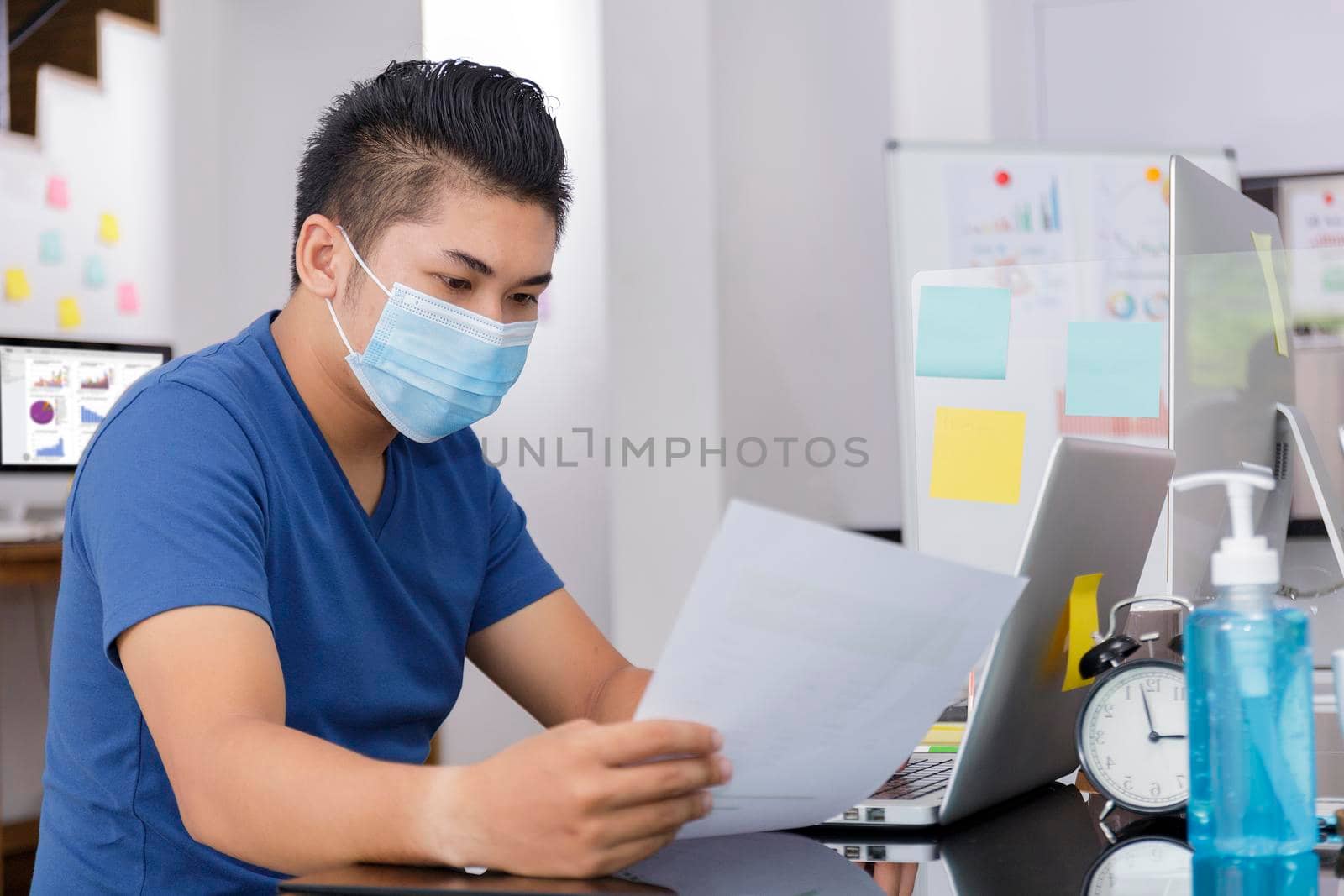 Asian small business start up working at Private Home Office social distancing among Coronavirus outbreak. Businessman wear face mask holding document paper chart .