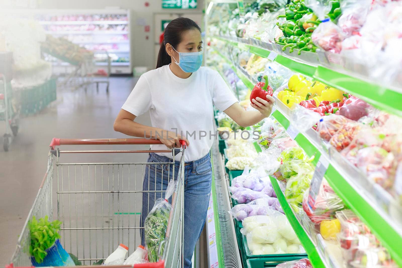 Asian woman wear face mask push shopping cart in supermarket. Girl looking grocery to buy something During coronavirus crisis or covid19 outbreak. Women wearing protective face mask new normal concept