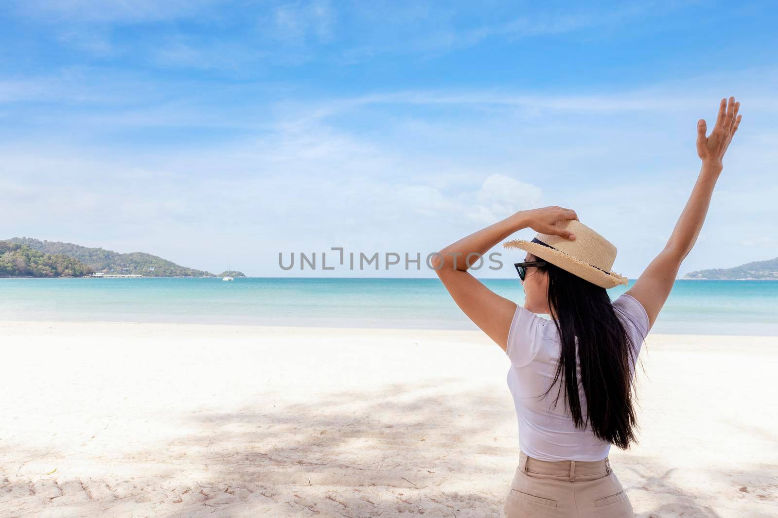 Portrait  middle shot view of woman stand in white T shirt and hat looking out towards blue ocean and sky, Women enjoy with beautiful sea view. Summer holiday vacation time