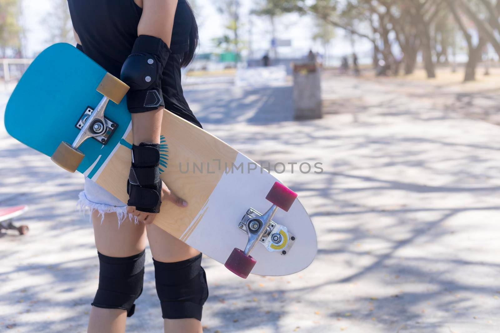 Close up on young women wear protection and hand hold skateboard, surf skate on public skate ramp park background. Free relax skateboard surf skate trendy concept. Fashion portrait of female hands holding surf skateboard