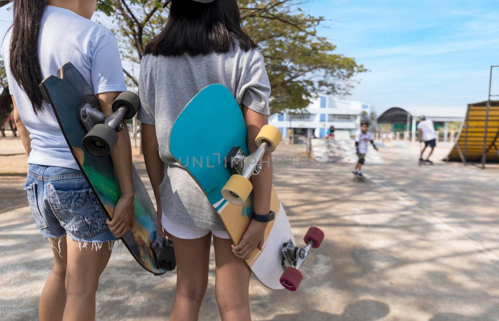 Two girl hand hold skateboard, surf skate on public skate ramp park background. Free relax skateboard surf skate trendy concept. Fashion portrait of female hands holding surf skateboard by Satrinekarn