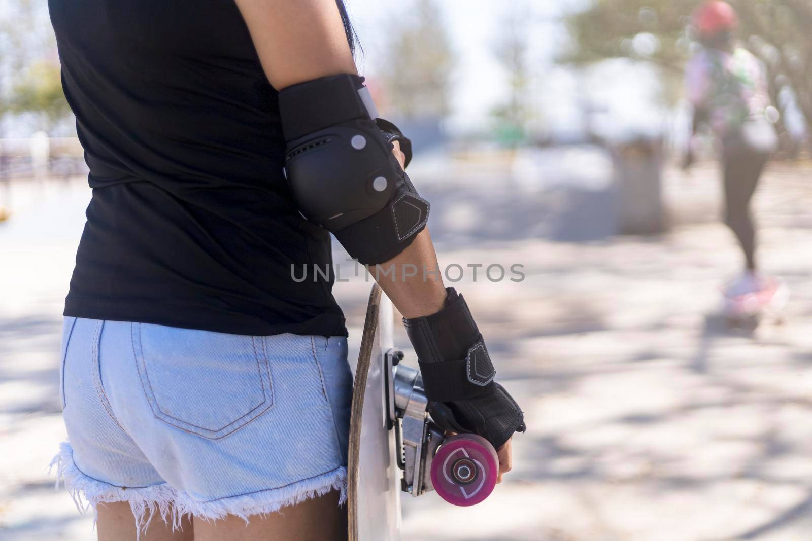 Close up on young women wear protection and hand hold skateboard, surf skate on public skate ramp park background. Free relax skateboard surf skate trendy concept. Fashion portrait of female hands holding surf skateboard