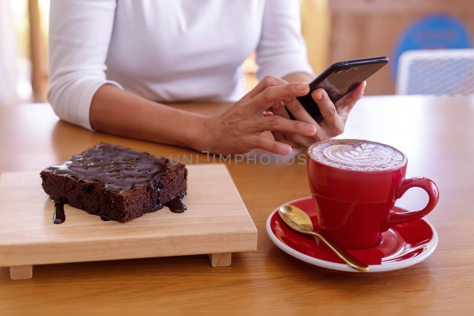 Woman hands holding mobile smart phone sitting in cafe with cup of coffee and brownies dessert. Women relax or working with cell phone in coffee shop with hot cappuccino and dessert. 