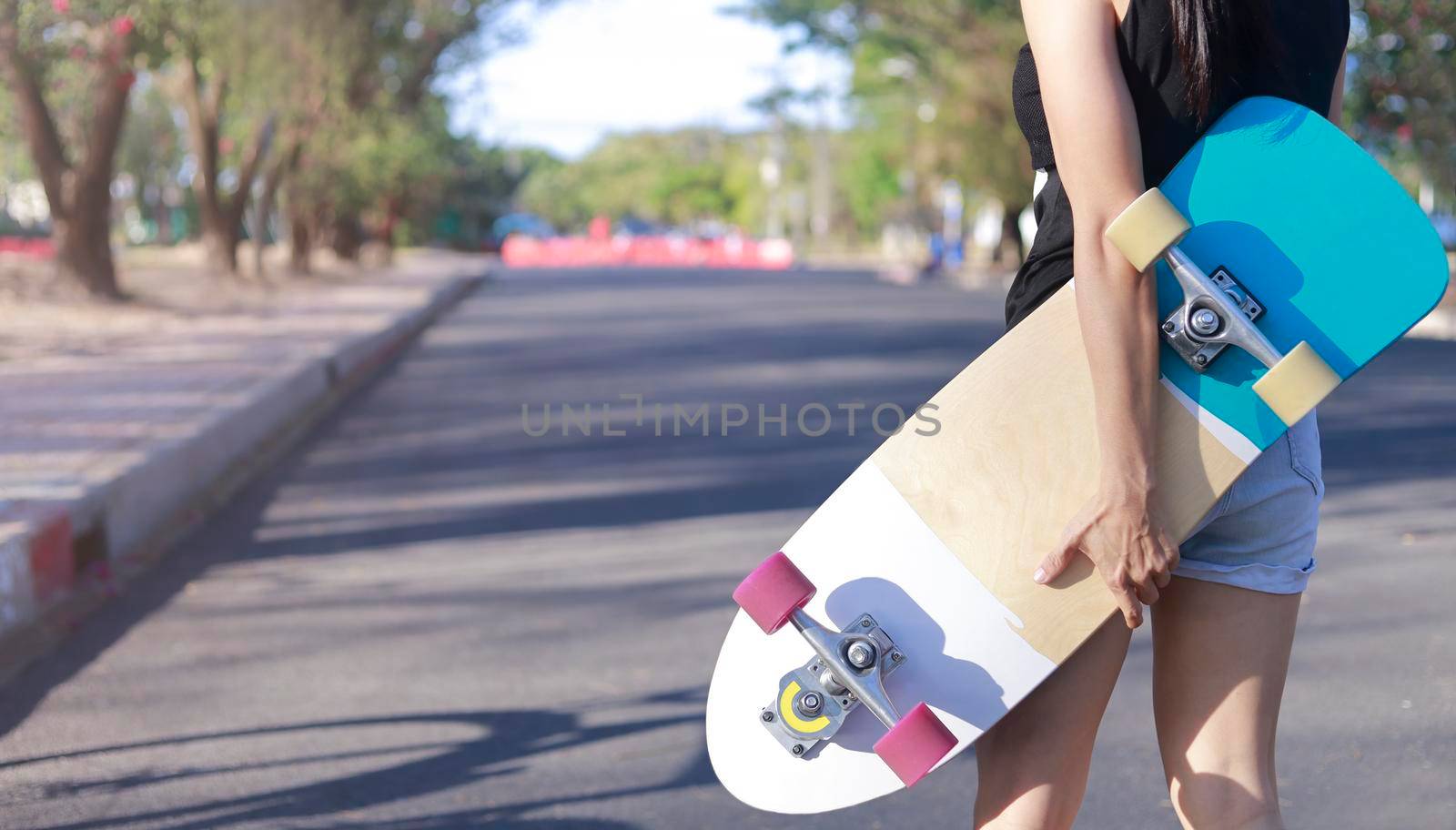 Close up on young women hand hold skateboard, surf skate on public park background. Free relax skateboard trendy concept. Fashion portrait of female hands holding surf skateboard by Satrinekarn