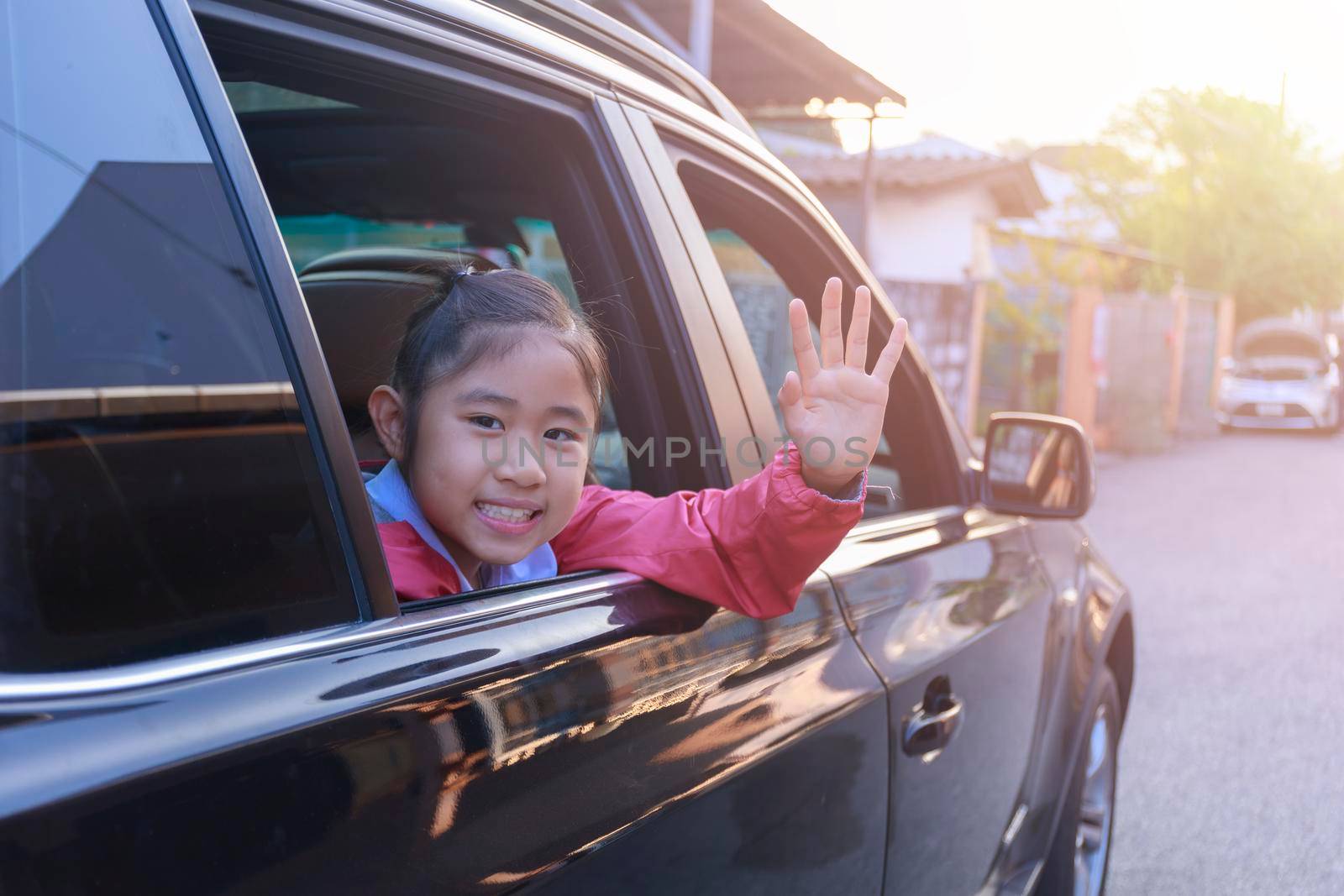 On the way to school, the little girl stretched out his hand from the car window, laughing and smiling. Asian little girl smiling  and waving hand out the car. Children relax with street view from the car. Family in car concept.