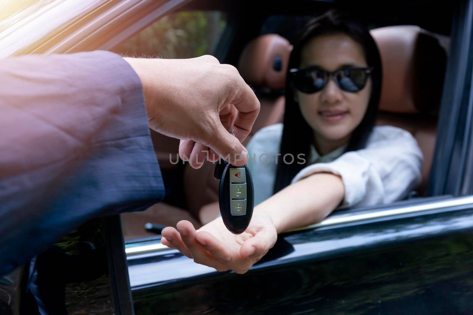 Close up of dealer giving key to new owner car. New car. Auto dealer giving woman automobile key for test drive on country road. Soft focus  smiling women try to test drive a car on road with dealer.