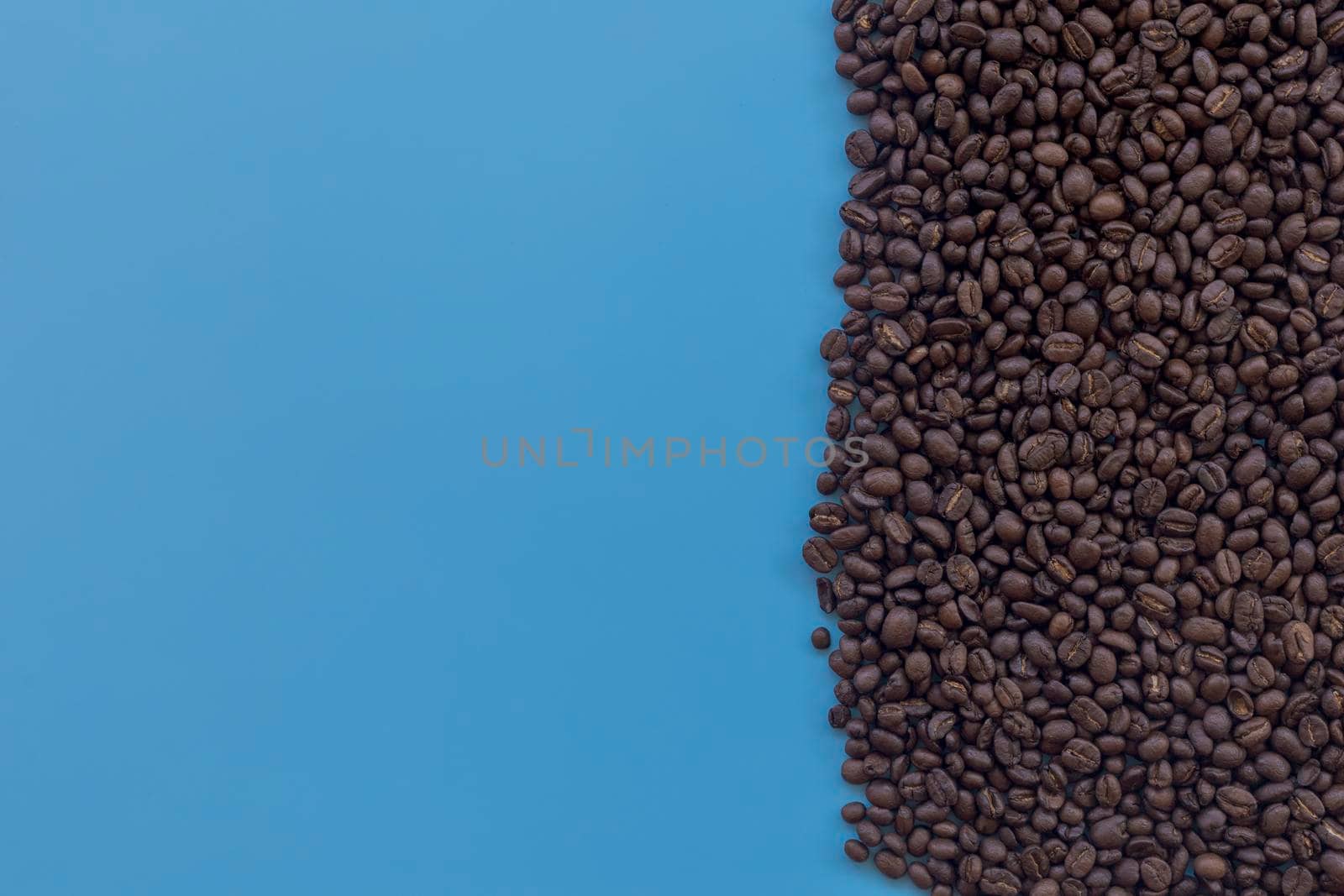 Top view brown roasted coffee beans scattered on blue background. Coffee beans on half of blue background with copy space