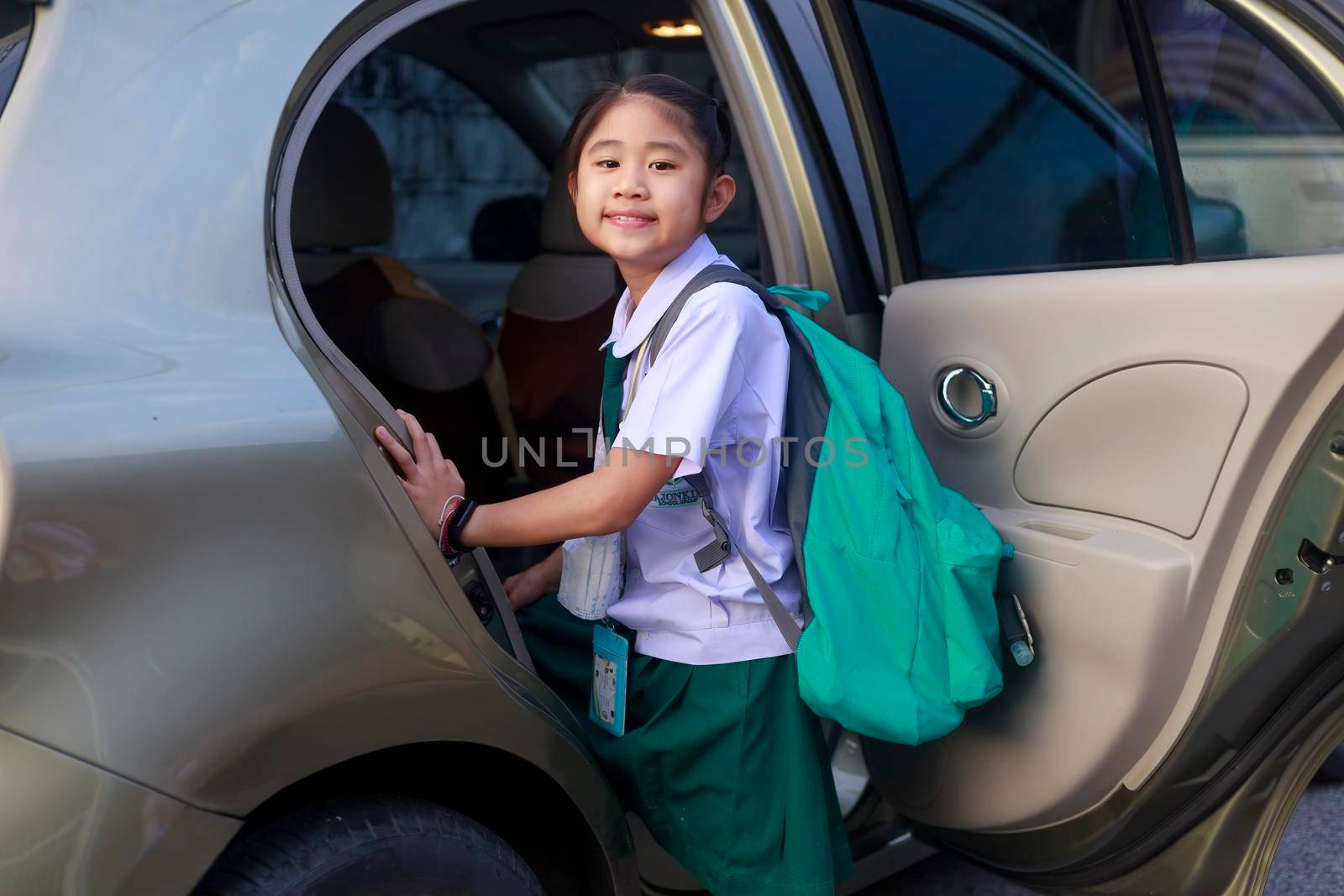 Asian School girl Wear school uniform And carrying a green backpack Getting on the bus to go to school in the morning. Happy primary school child get in car. Family in car transportation concept. by Satrinekarn