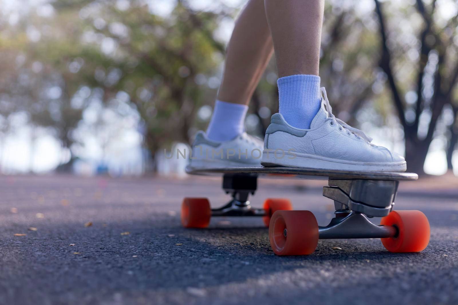 Close-up Asian women surf skate or skateboard outdoors on beautiful morning. Happy young women play surf skate at park on morning time. Close up Asian women leg wear sneaker paly surf skate on public park. Sport concept