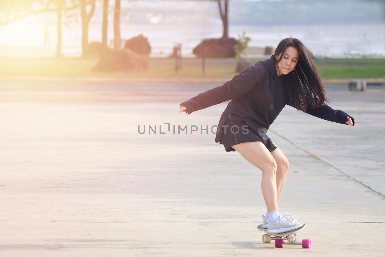 Asian women on skates board outdoors on beautiful summer day. Happy young women play surfskate at park on morning time. Sport activity lifestyle concept