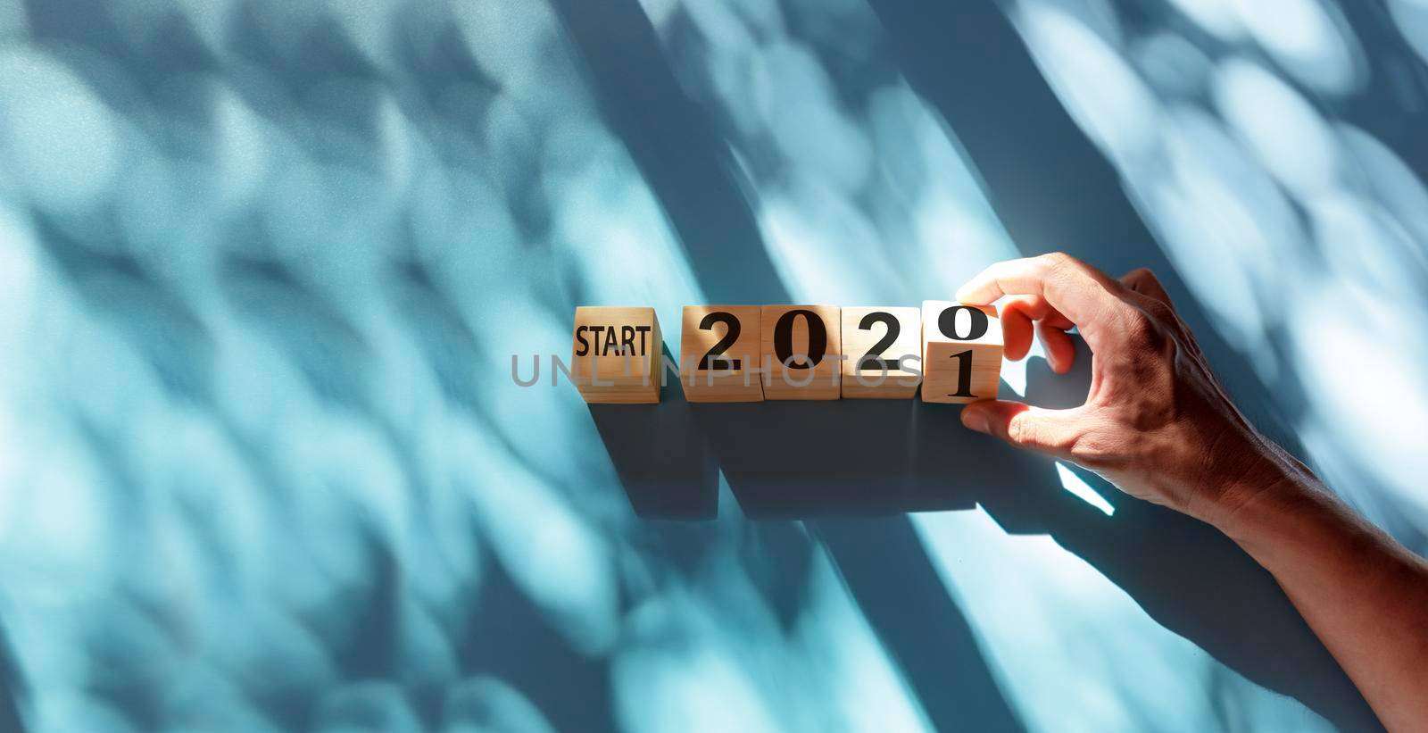 Hand holding wooden cube with flip over block start 2020 to 2021 word on blue and shadow background. Top view hand flip wood block with number text start 2020, 2021 with copy space