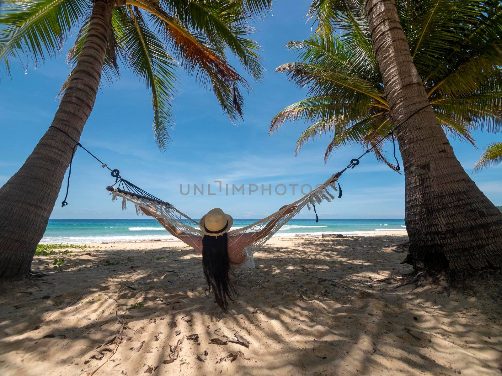Phuket Thailand. Asian young woman relaxing on hammock by the beach at sunset. Young attractive female swinging on hammock. Holiday vacation summer