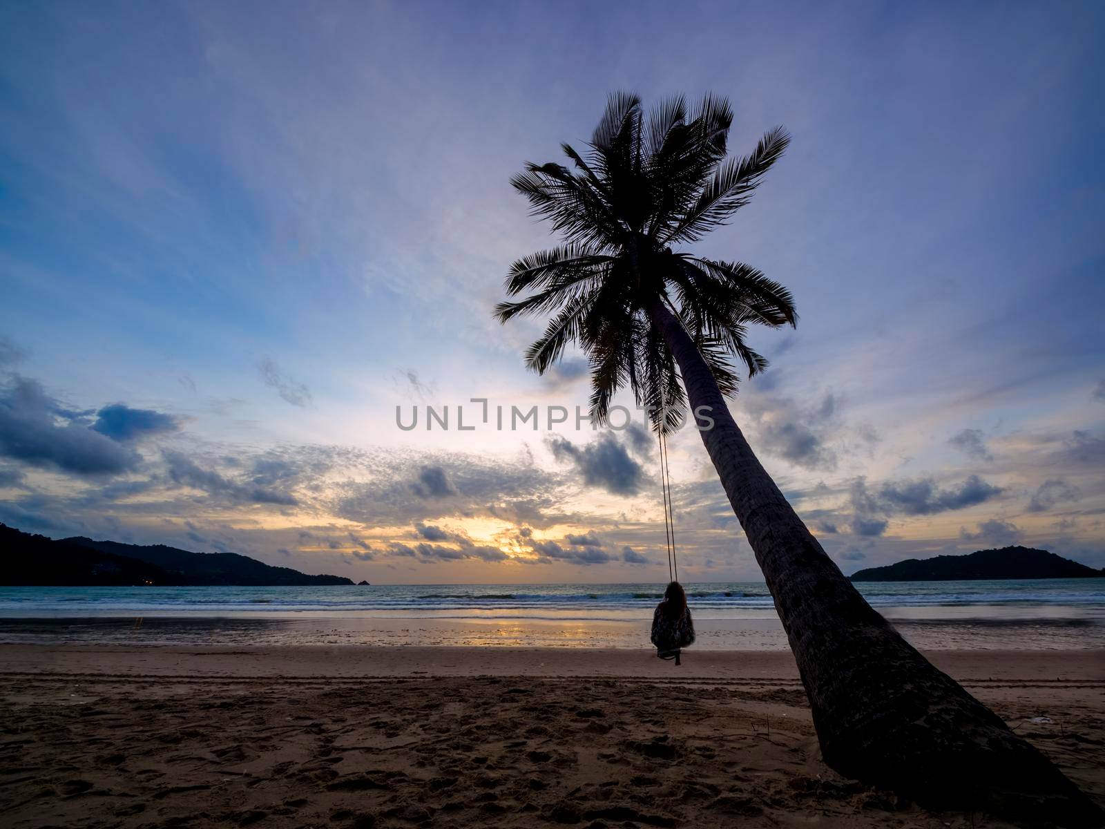 Phuket, Thailand. Tropical beach paradise with beach swing with women sitting. sunset with silhouette women relax on swing under coconut palm tree at beautiful tropical beach vacation summer holiday concept