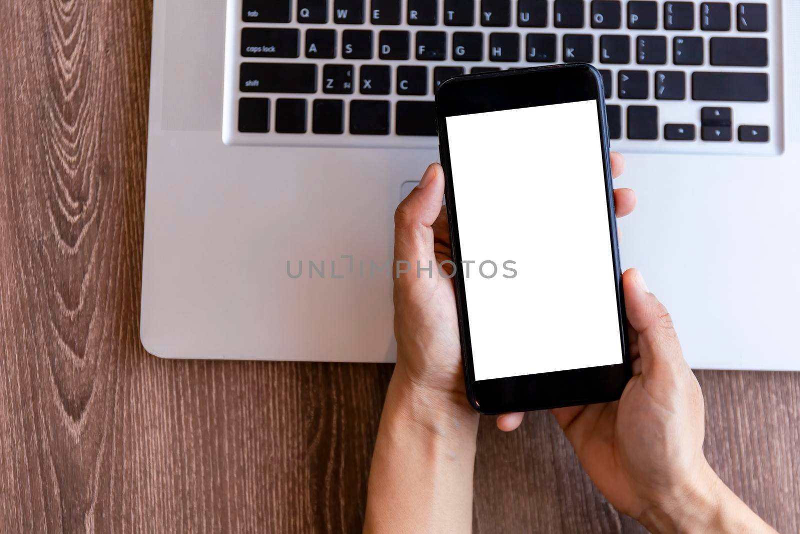 Top view female hands holding smart phone with blank white screen. Women hands workspace, close-up hand holding smartphone blank screen for text and content on wood table background.