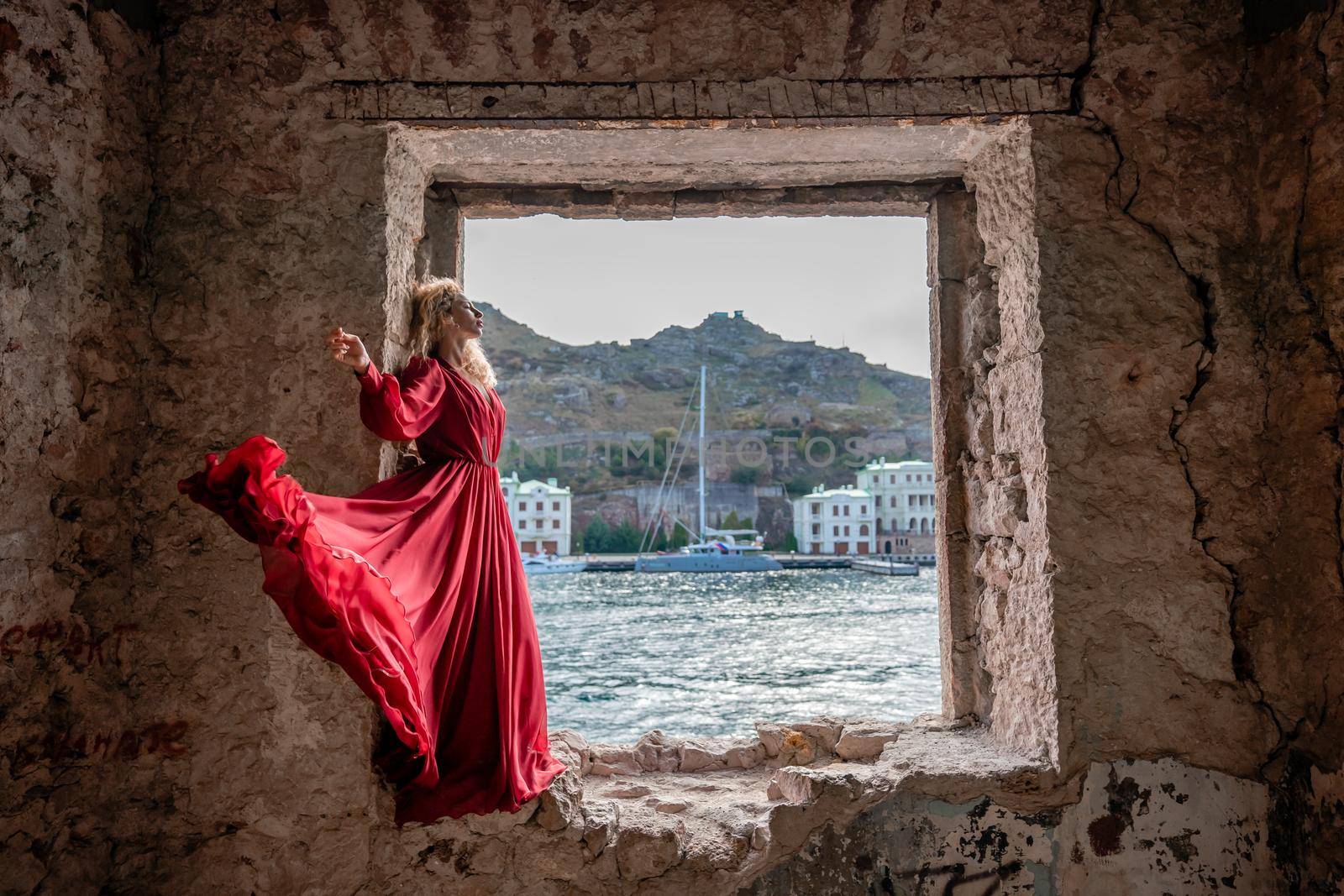 View of Balaklava Bay through an arched balcony in oriental style. The girl in a long red dress stands with her back. Abandoned mansion on the Black Sea coast.