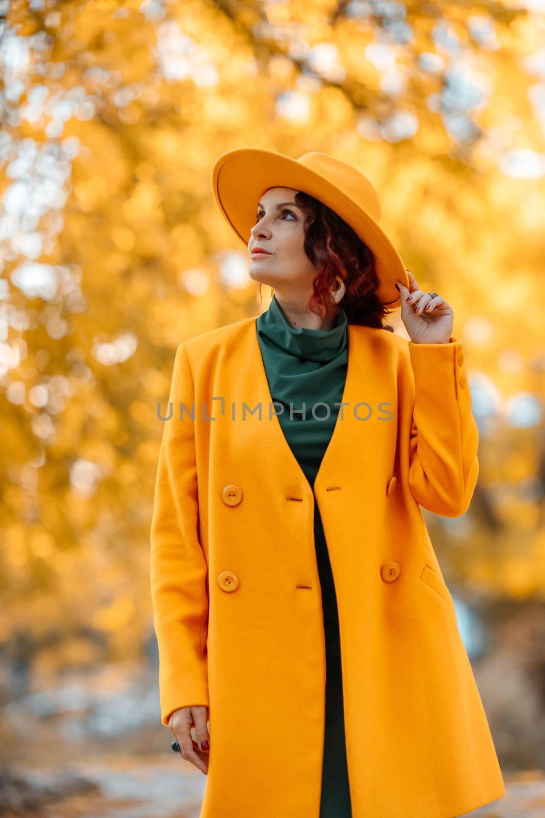 Beautiful woman walks outdoors in autumn. She is wearing a yellow coat, yellow hat and green dress. Young woman enjoying the autumn weather. Autumn content.