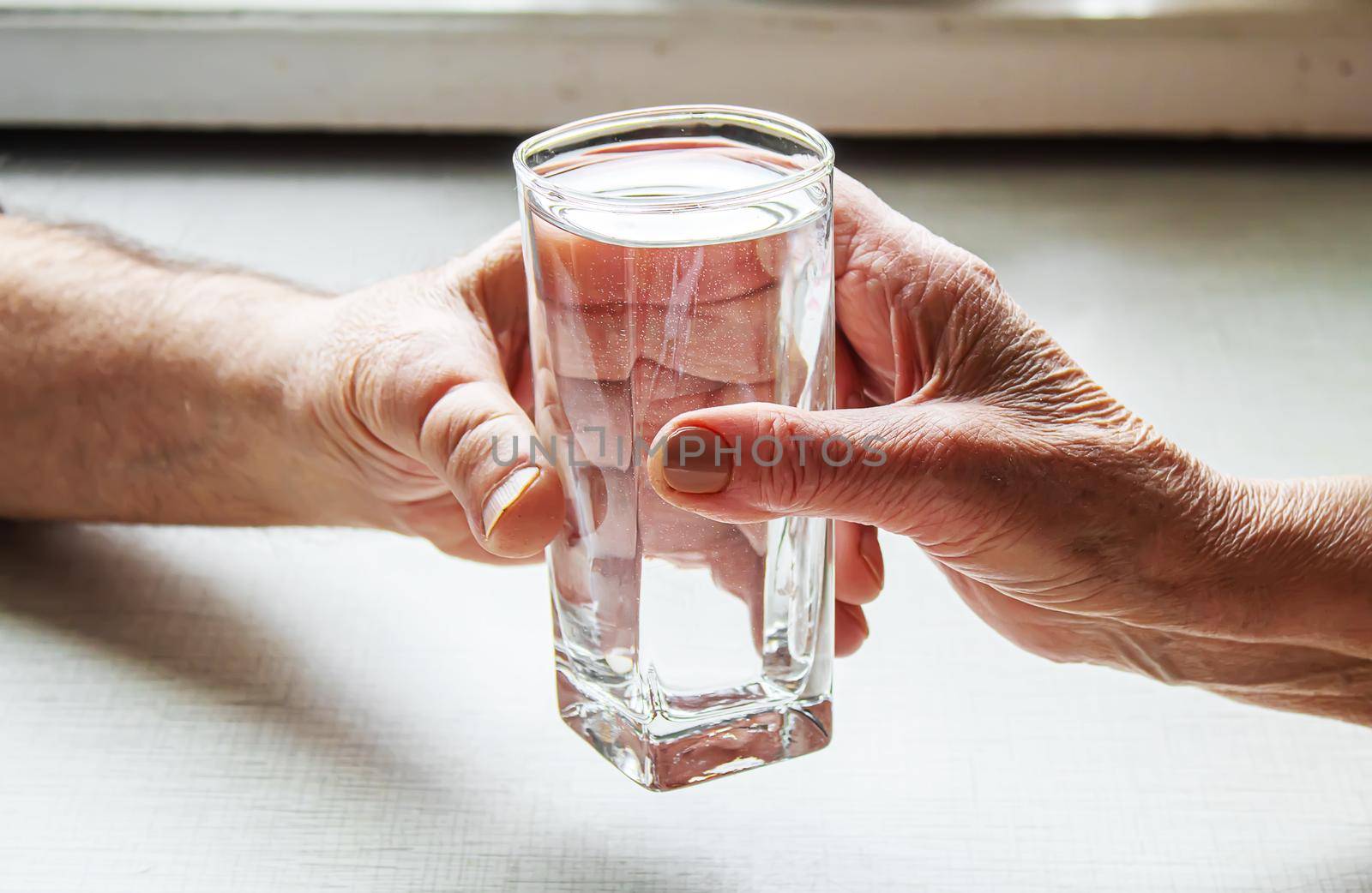 Grandma gives grandfather a glass of water. Selective focus. by mila1784
