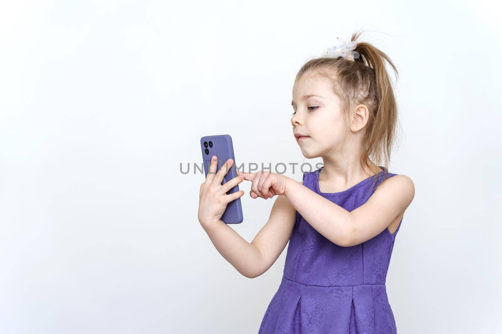 cute 5-6 year old girl in a blue dress posing in the studio with a smartphone