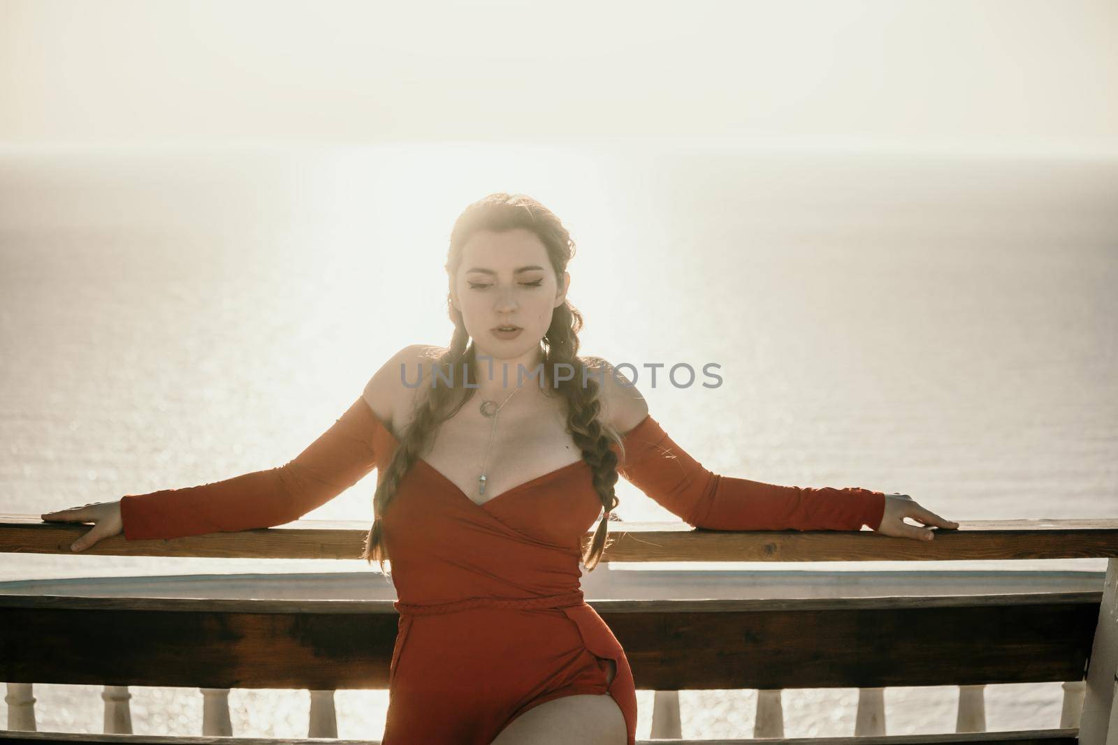Closeup portrait of sensual young brunette woman in red dress, happily dancing outdoors isolated on blurry sea background with natural bokeh in soft warm sunset backlight. Selective focus. by panophotograph