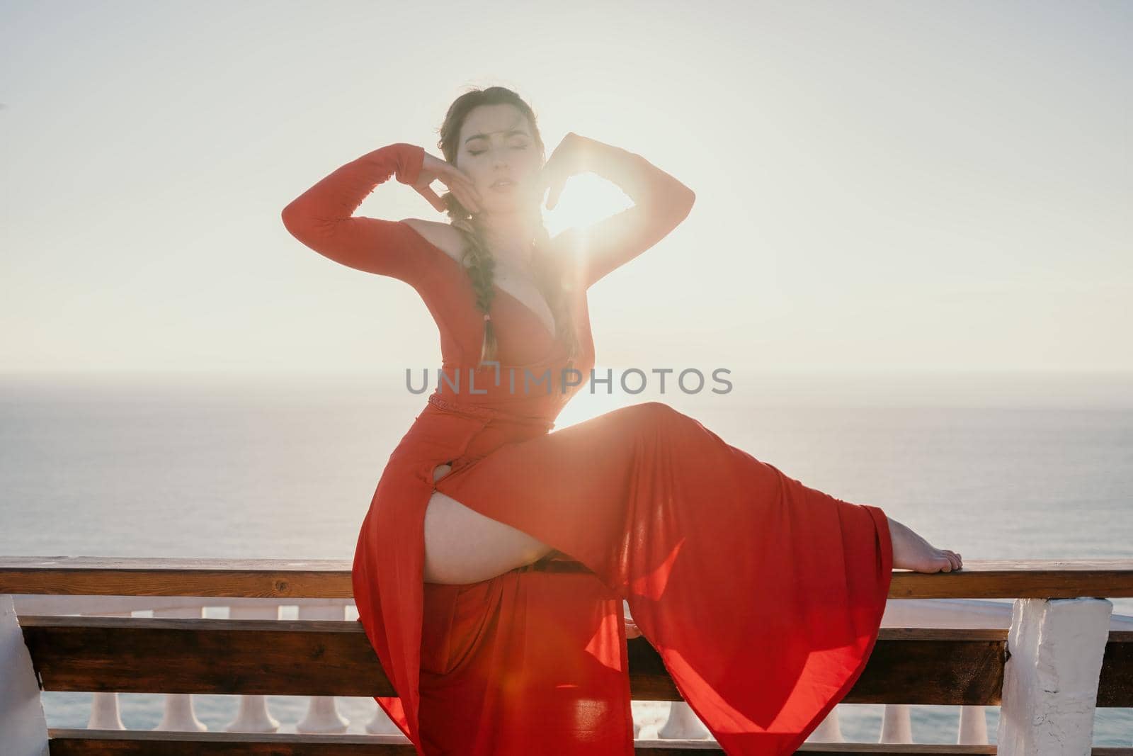 Closeup video portrait of sensual young brunette woman in red dress, happily dancing outdoors isolated on blurry sea background with natural bokeh in soft warm sunset backlight