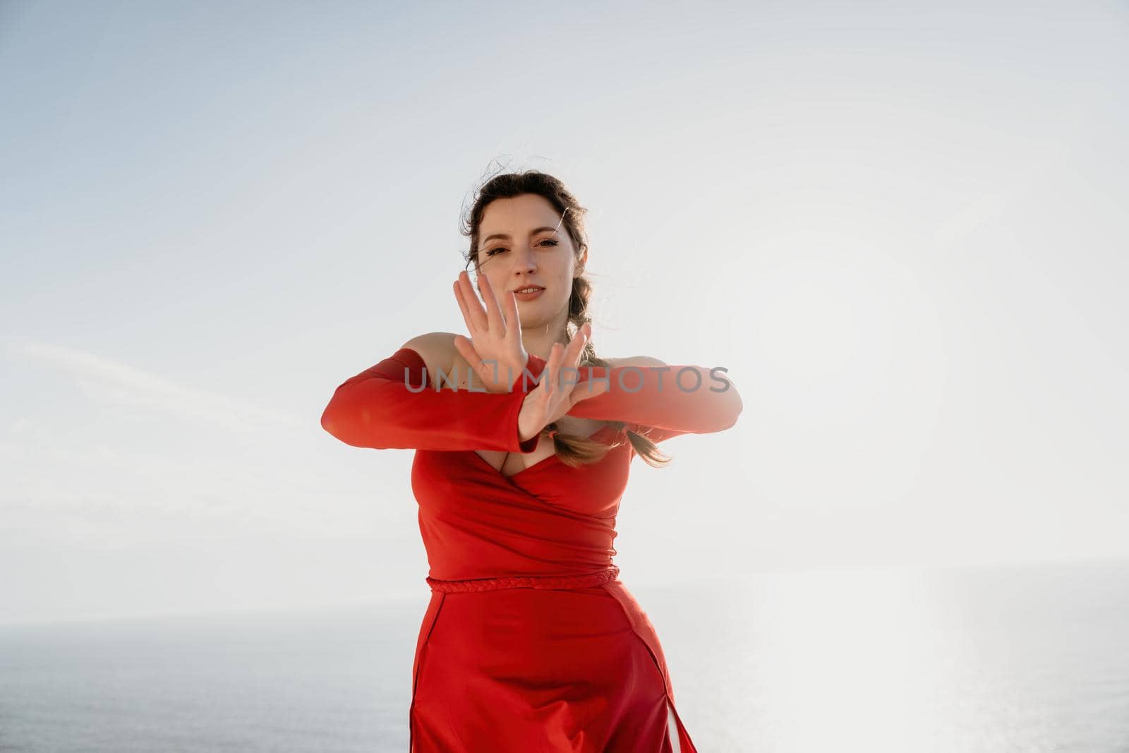 Closeup video portrait of sensual young brunette woman in red dress, happily dancing outdoors isolated on blurry sea background with natural bokeh in soft warm sunset backlight