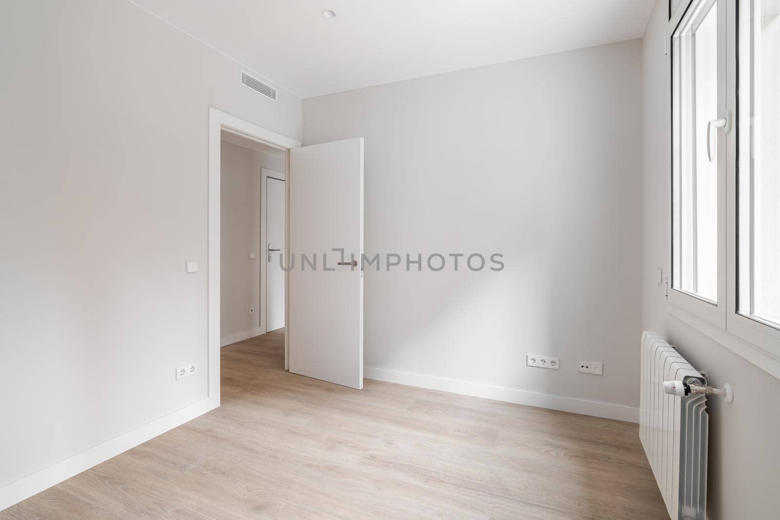 Empty room with door, window, and heating radiator in a white interior house.