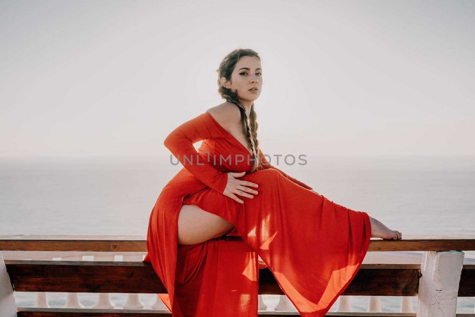 Closeup video portrait of sensual young brunette woman in red dress, happily dancing outdoors isolated on blurry sea background with natural bokeh in soft warm sunset backlight