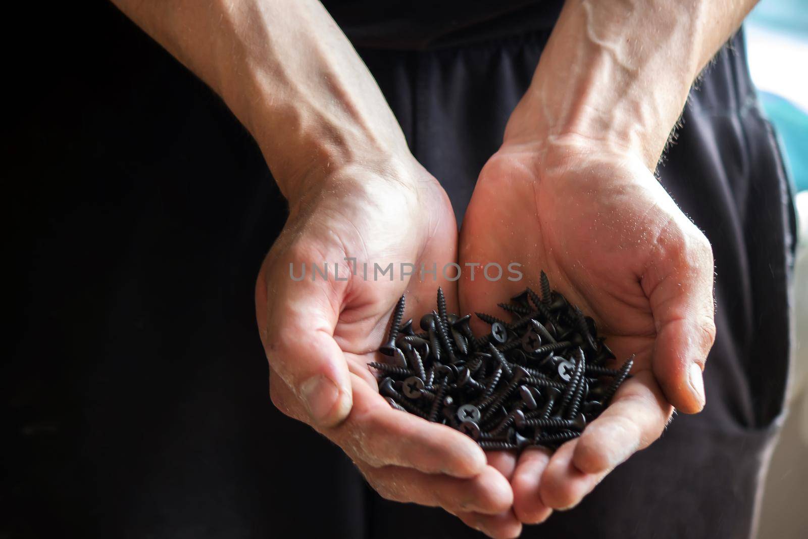 Black small self tapping screws for steel profile of drywall on young adult man hand on light gray table background. Opened palm. Closeup.