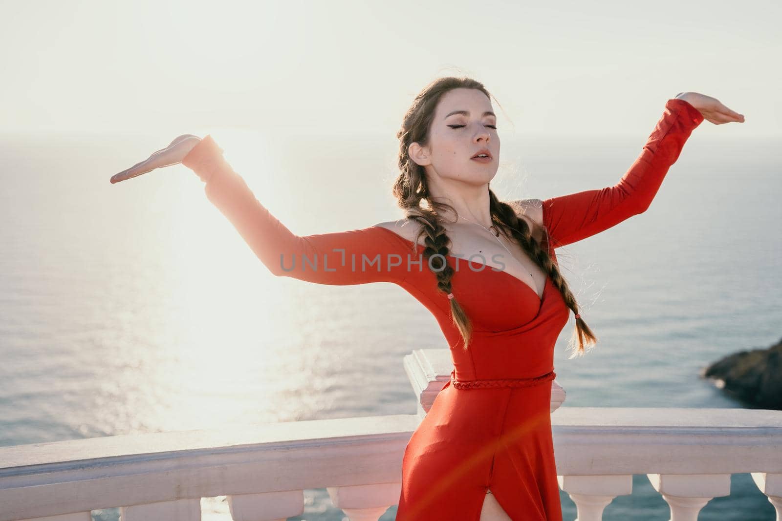 Closeup video portrait of sensual young brunette woman in red dress, happily dancing outdoors isolated on blurry sea background with natural bokeh in soft warm sunset backlight