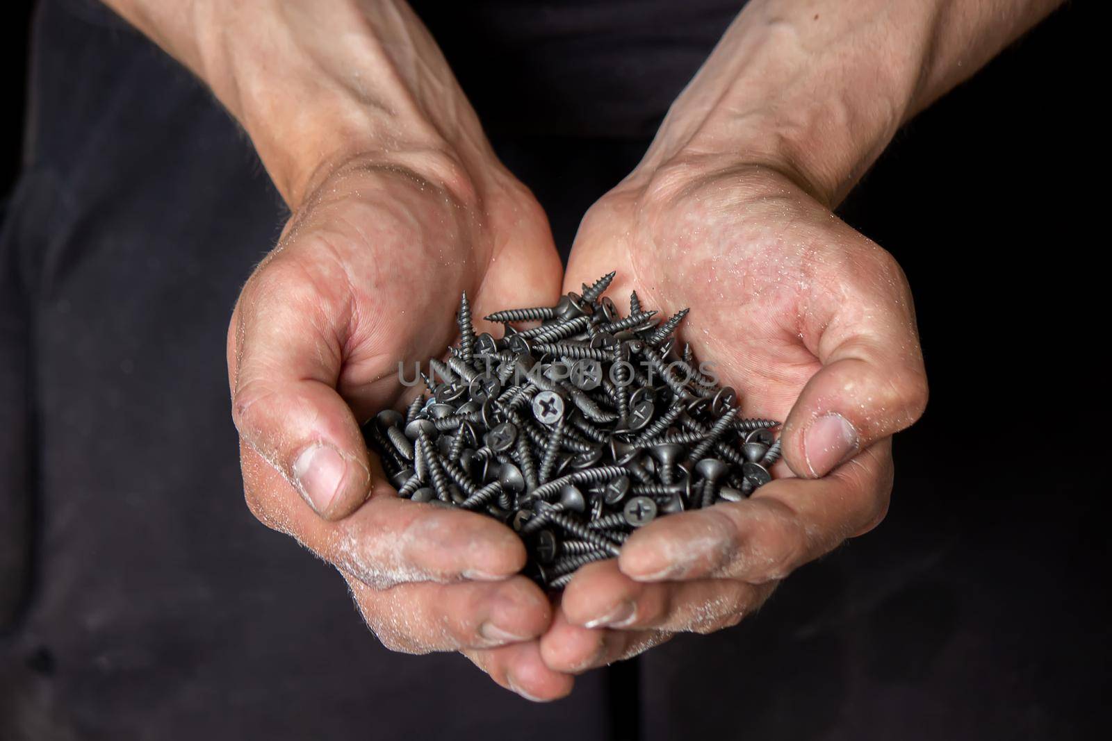 Black small self tapping screws for steel profile of drywall on young adult man hand on light gray table background. Opened palm. Closeup.