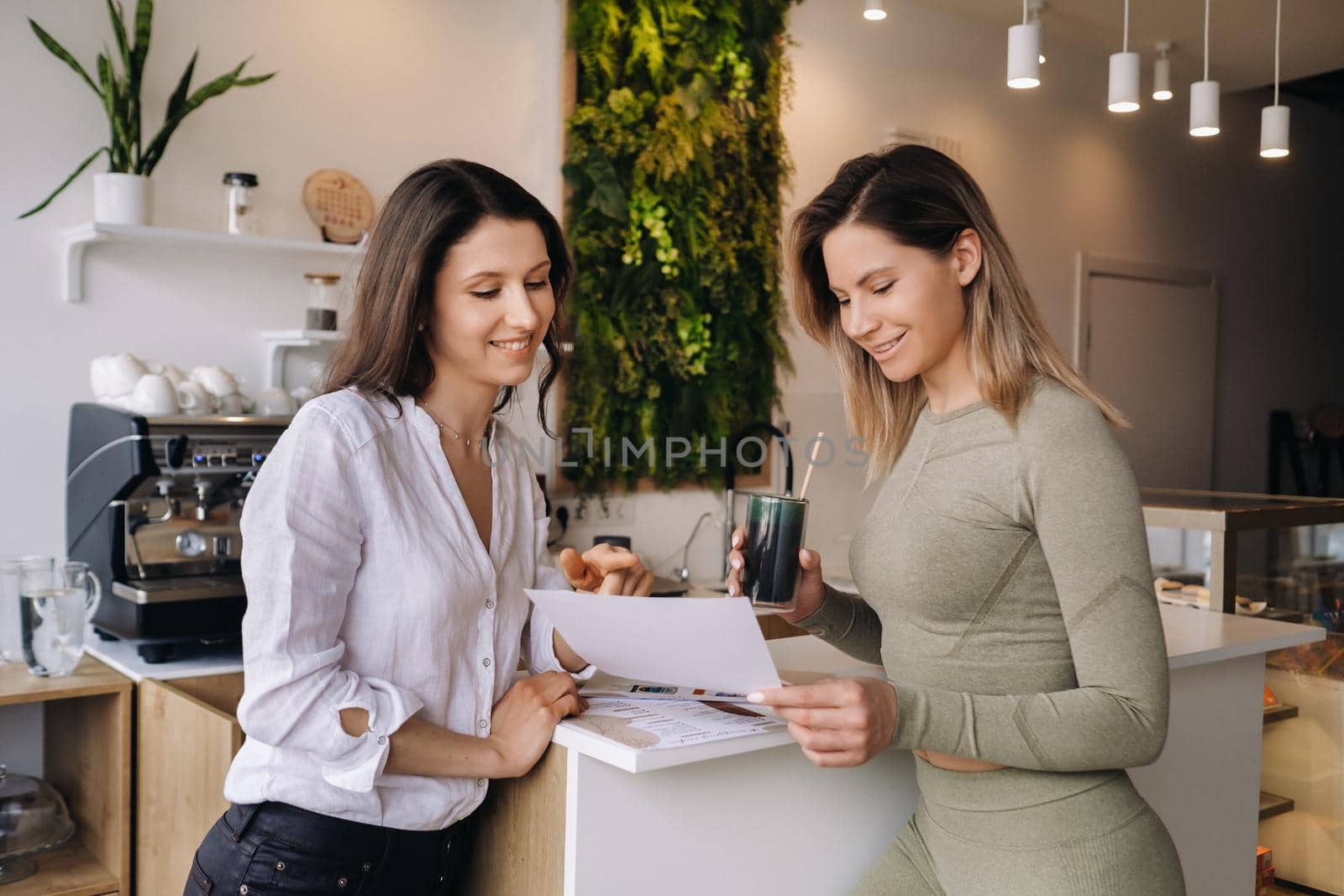 A nutritionist and a girl after fitness classes discuss healthy eating standing in a cafe.