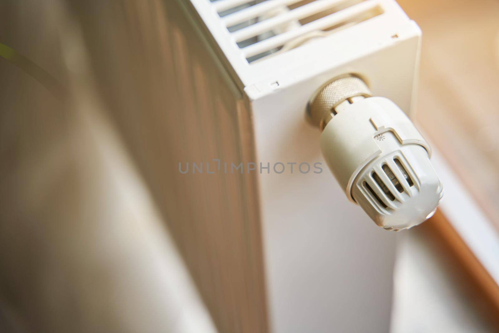 Radiator in the apartment. White heated battery. Thermostat head of a heating radiator in an apartment, office.