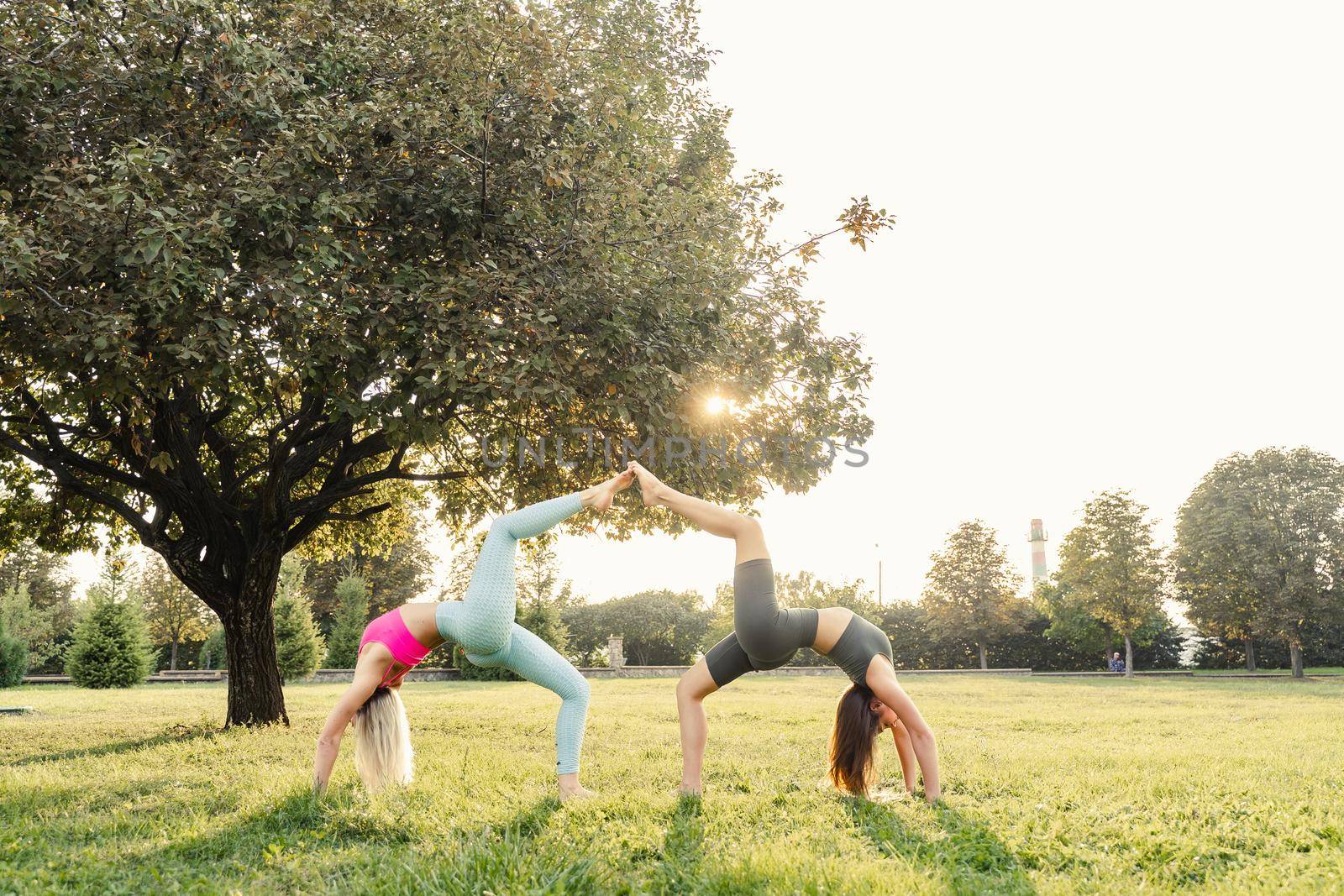 Sport gymnastics excercises of 2 girls outdoor in the green park. Gymnastics support exercise