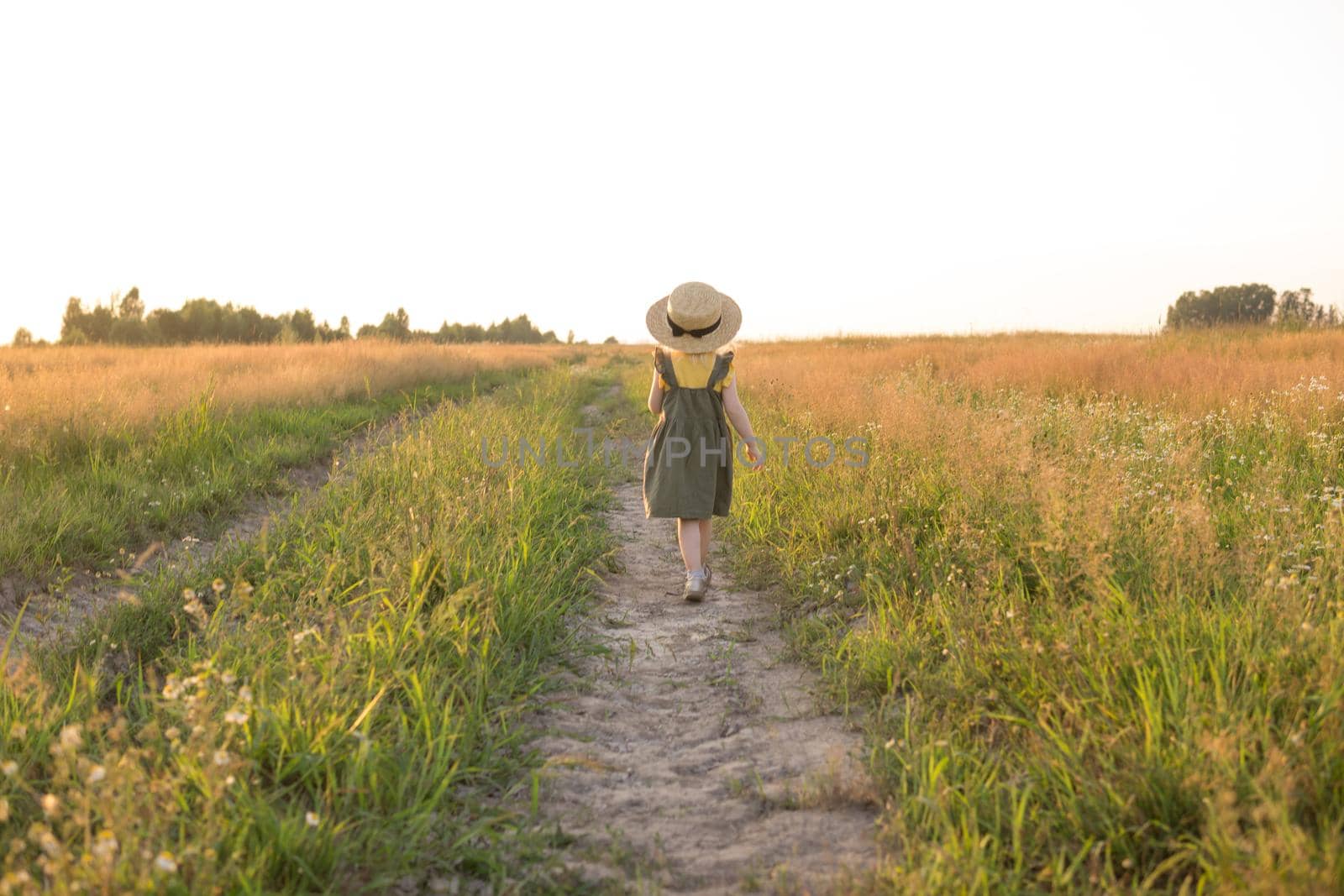 A little blonde girl in a straw hat walks in a field with a bouquet of daisies. The concept of walking in nature, freedom and an eco-friendly lifestyle