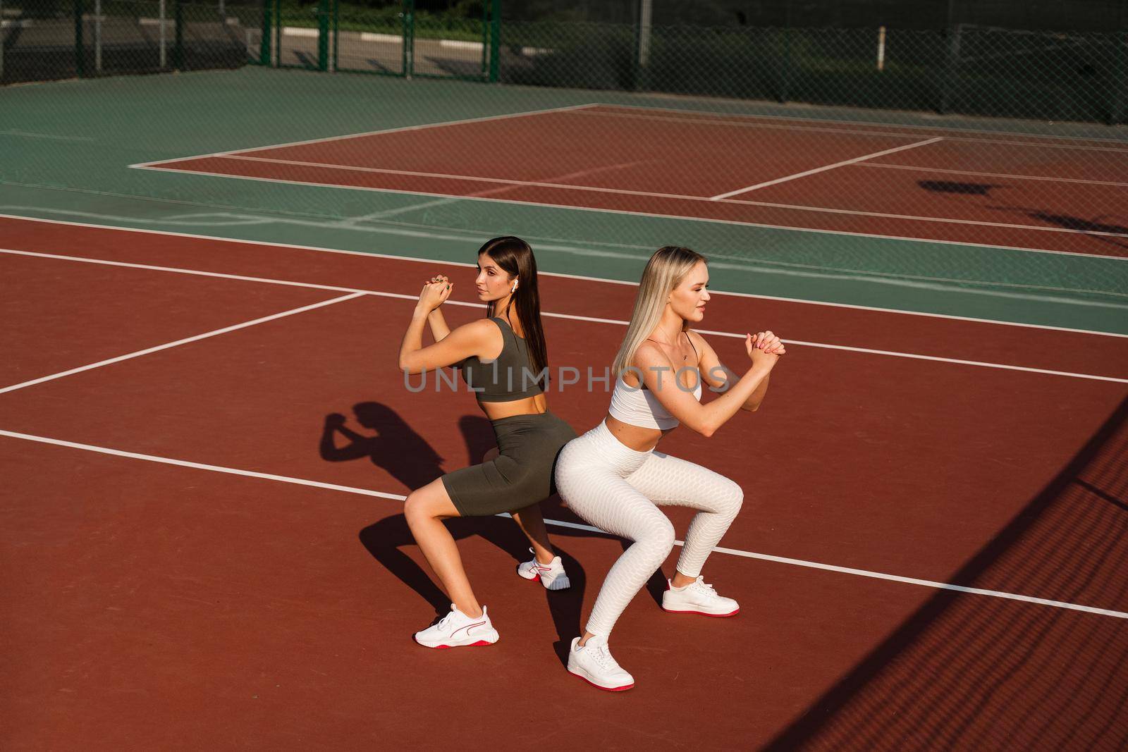 2 girls training outdoor together. 2 woman doing squat excercises