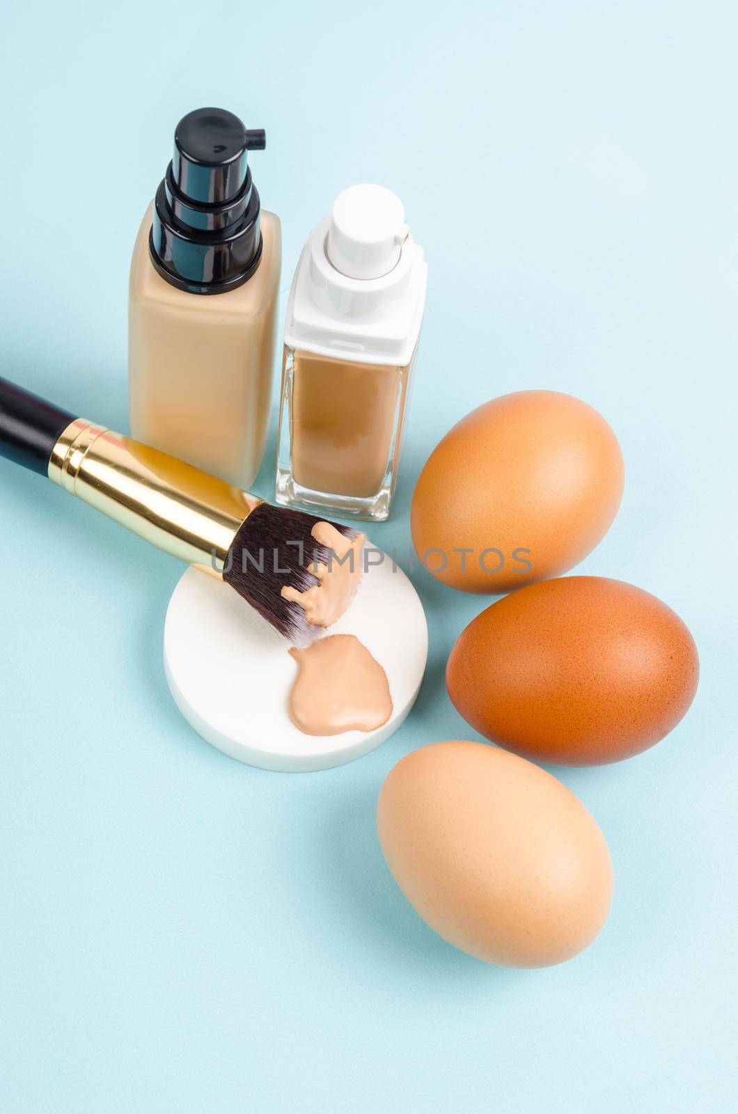 Liquid fluid foundation glass bottle on makeup sponges and egg on blue background. Choose tone color foundation makeup for skin concept. by Gamjai