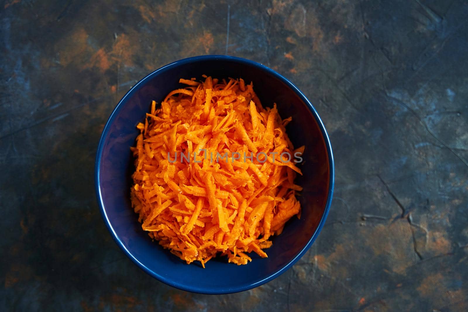 Grated carrots in a blue plate on a dark background. Carrot salad. Healthy breakfast.