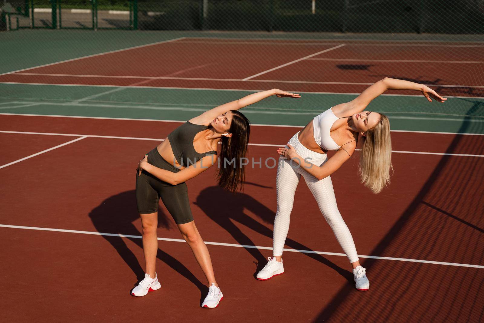 2 girls doing stretching before sports training. Outside group training. by Rabizo