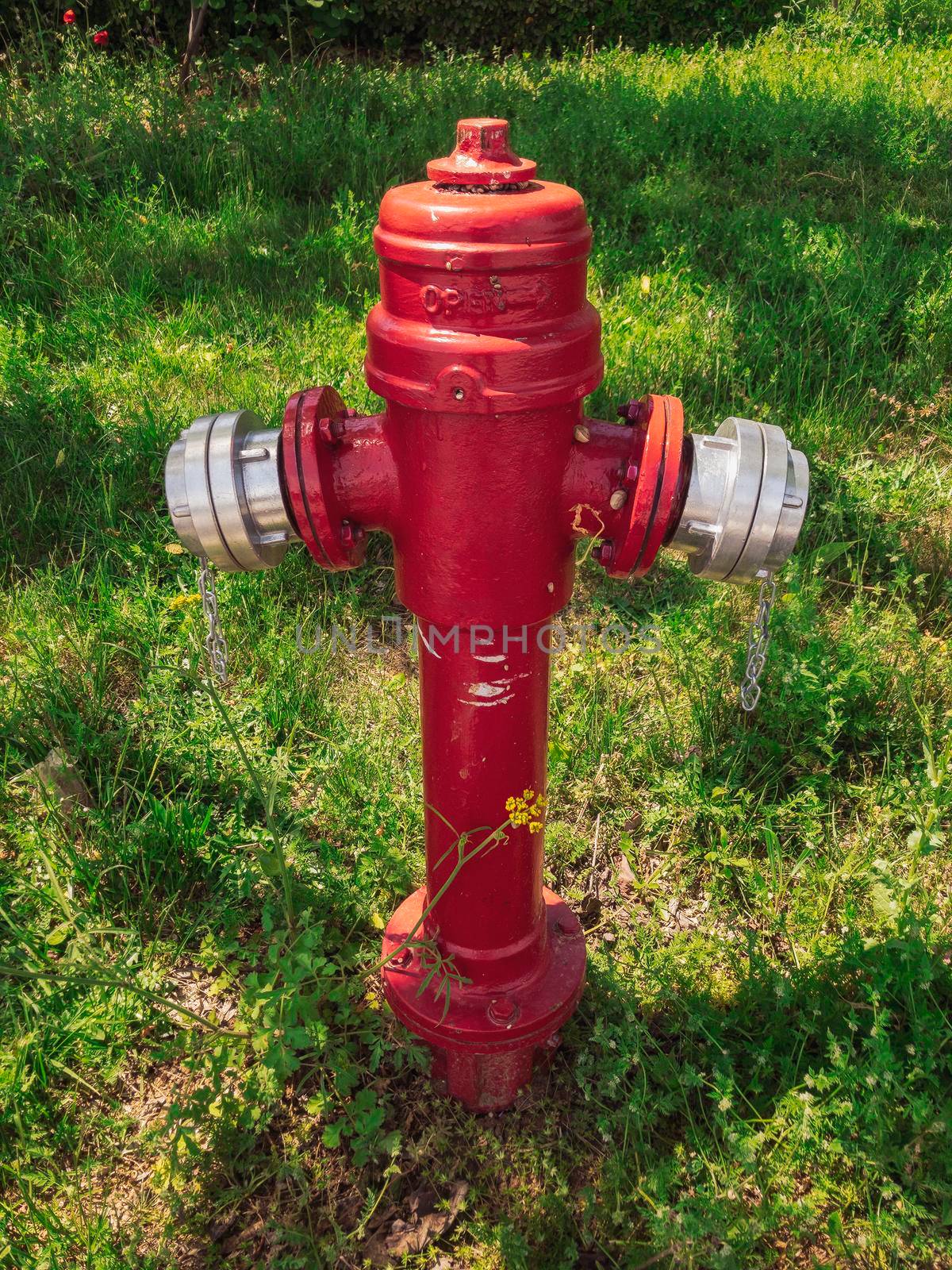 Red metal above ground water fire hydrant piping point against green vegetation at a rural environment.