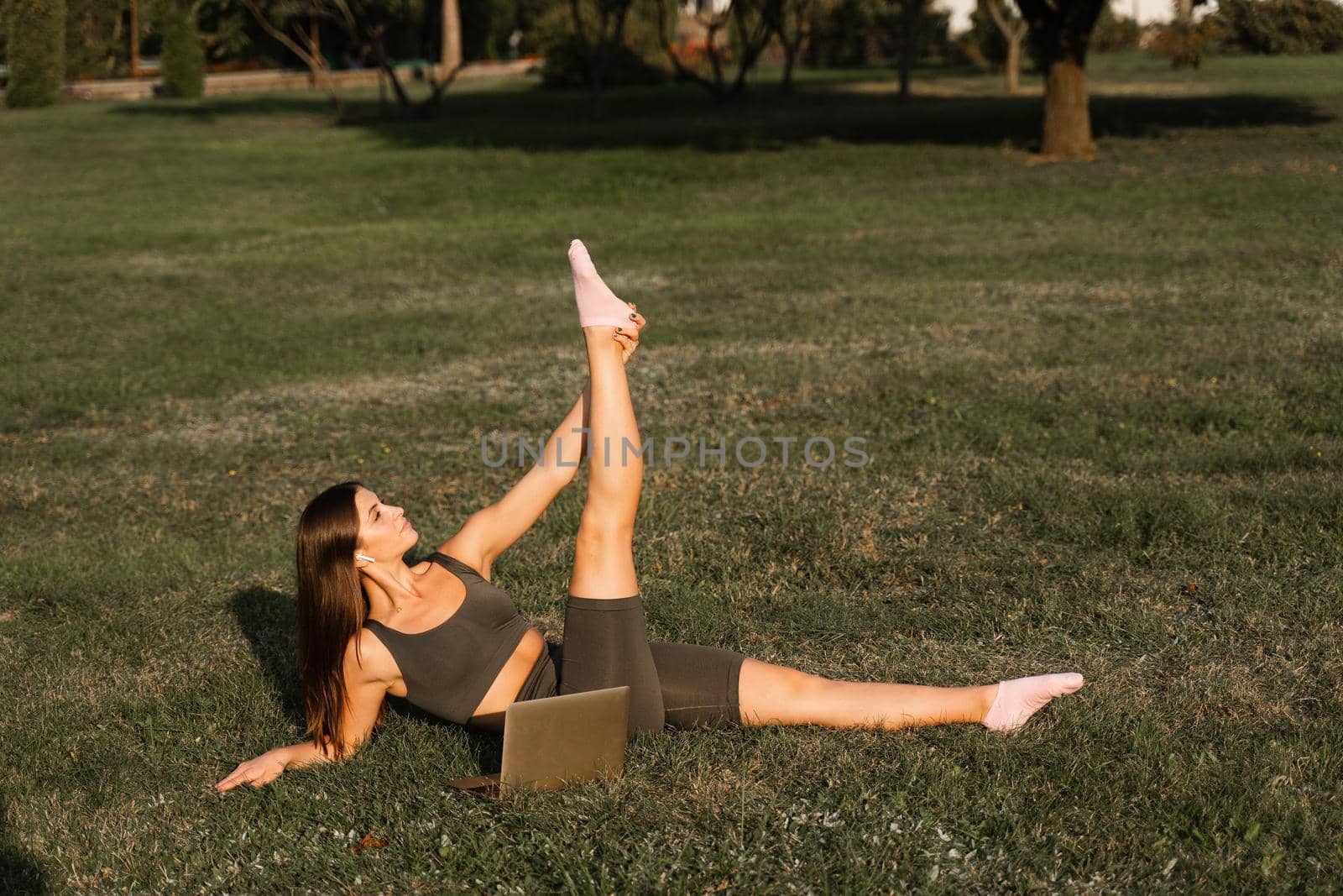 Online training with laptop in the green park. Active fit girl does fitness workout outdoor