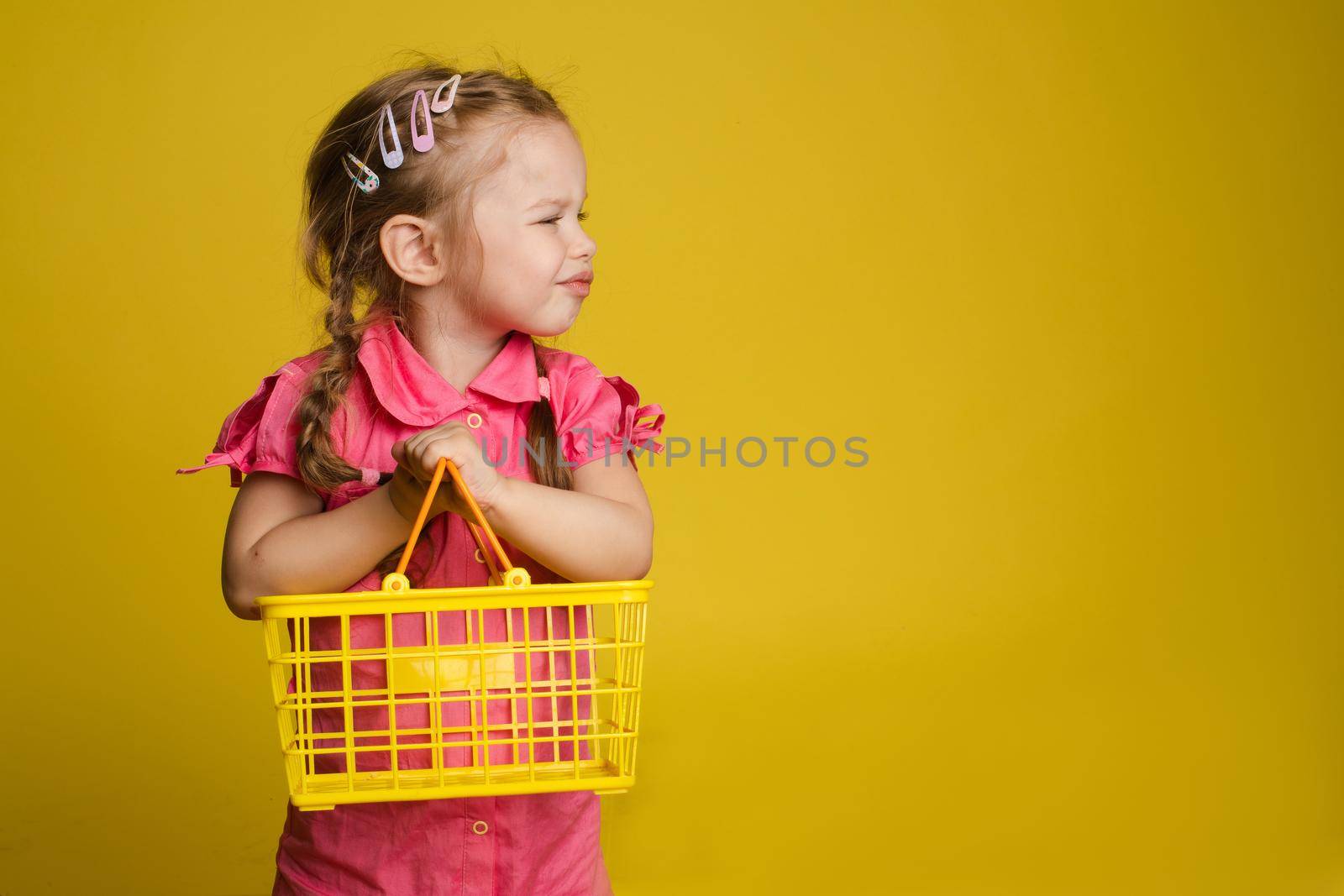 Cunning little cute girl holding small basket posing isolated at yellow studio background by StudioLucky