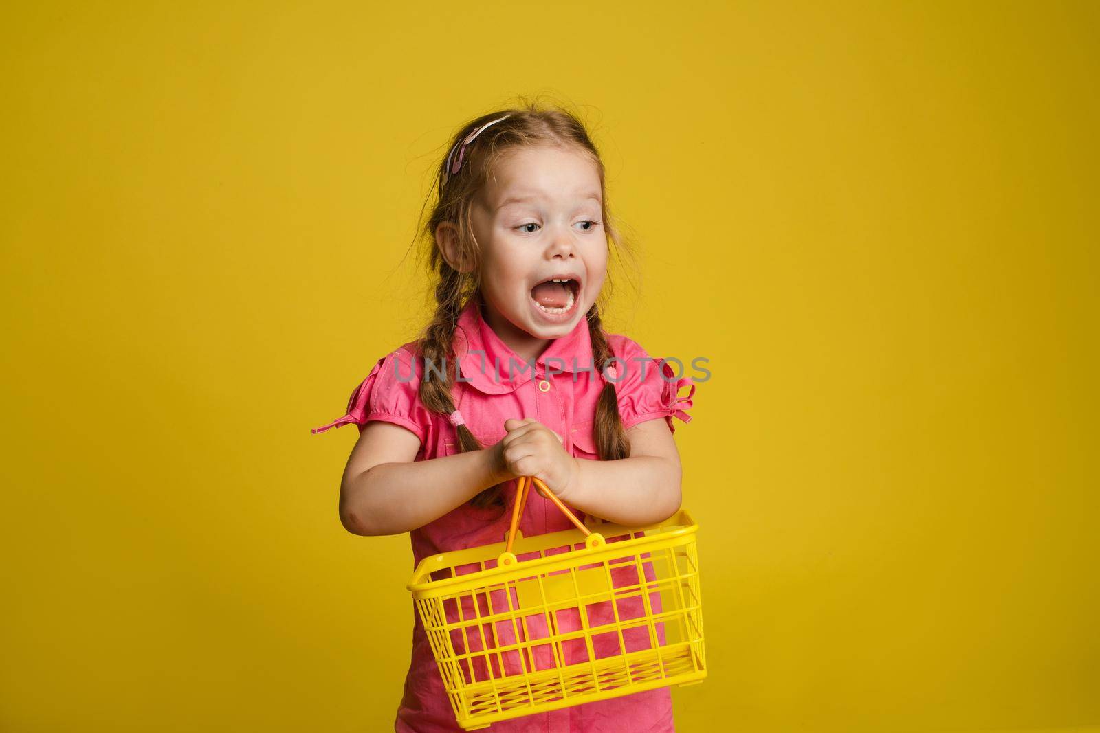 Funny little girl with shopping basket. Isolate on yellow background. by StudioLucky