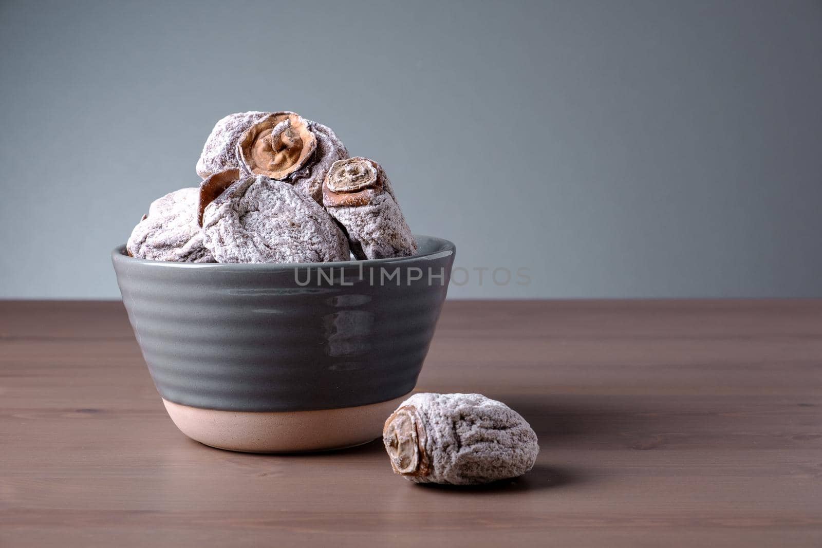 Several dried persimmons in ceramic bowl. This is useful product for diseases of endocrine and digestive systems, blood vessels, beriberi and anemia. Selective focus.