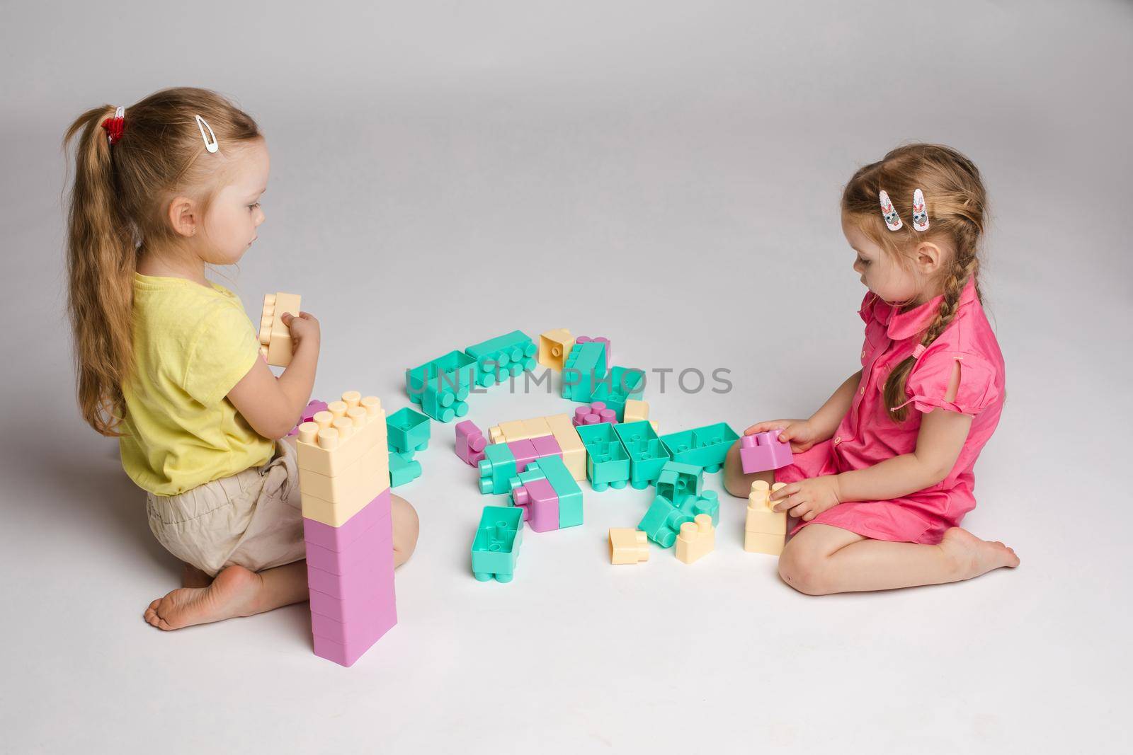 Two girls sitting on floor and playing with building blocks by StudioLucky