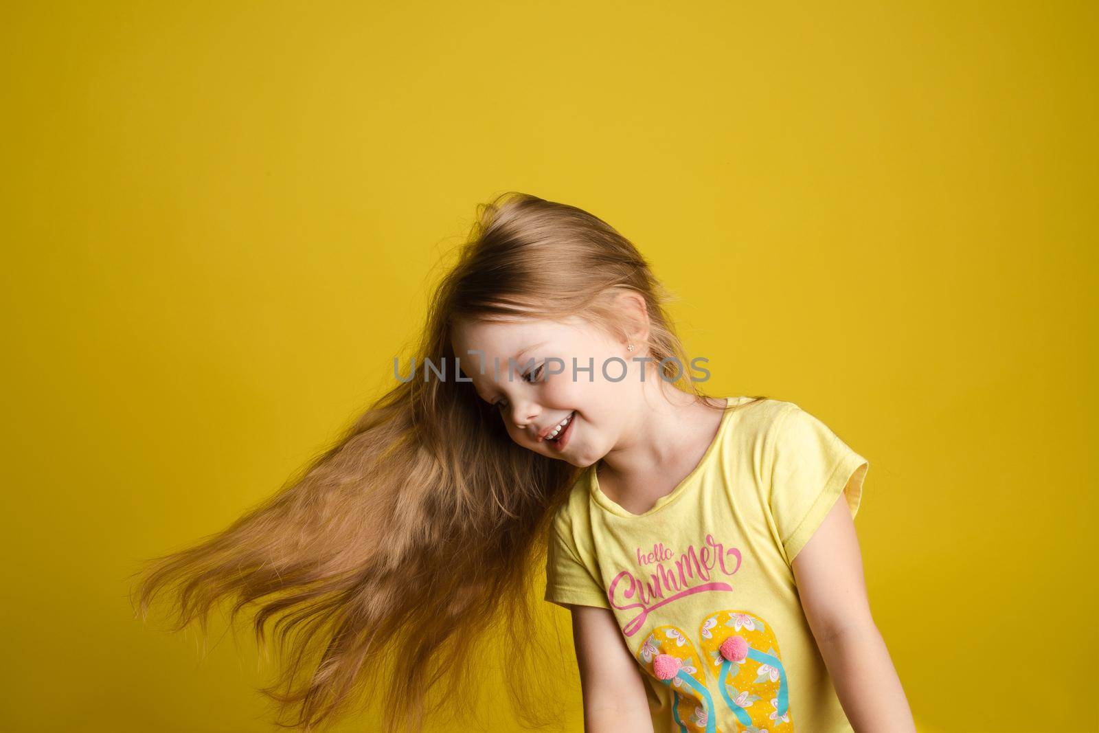 Portrait of beautiful little girl with long hair smiling posing isolated at yellow studio background medium shot. Happy cute European female child having fun looking at camera feeling positive emotion