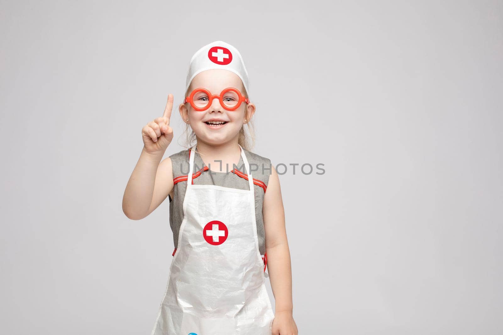 Cropped view of funny little girl wearing doctor uniform looking at camera and shoring sign of silence. Preschool child playing nurse and enjoying game on isoalted background. Concept of fun and joy.