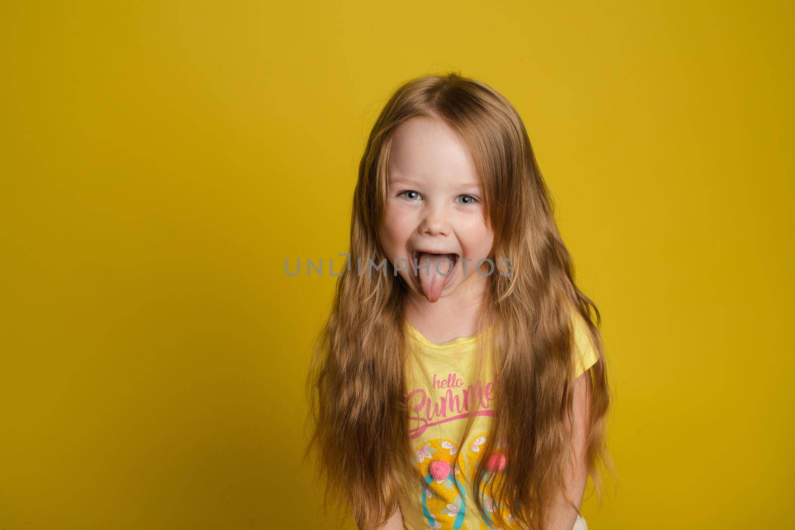 Portrait of beautiful little girl with long hair smiling posing isolated at yellow studio background medium shot. Happy cute European female child having fun looking at camera feeling positive emotion