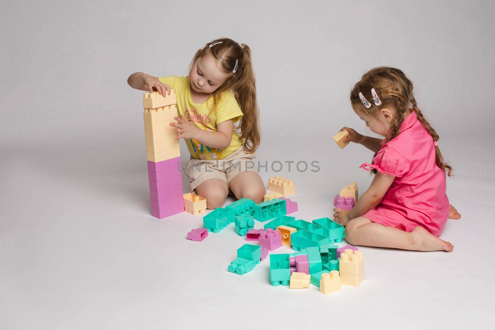 Two enthusiastic little girl playing assemble constructor full shot at studio white background by StudioLucky